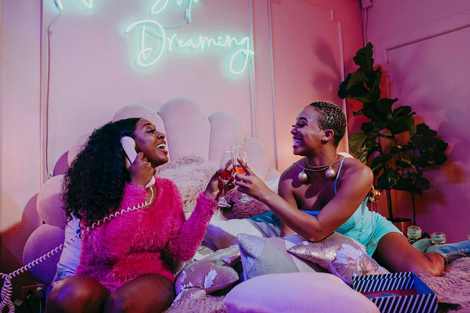 Two friends celebrating in a festive, vibrant indoor setting with drinks and laughter.